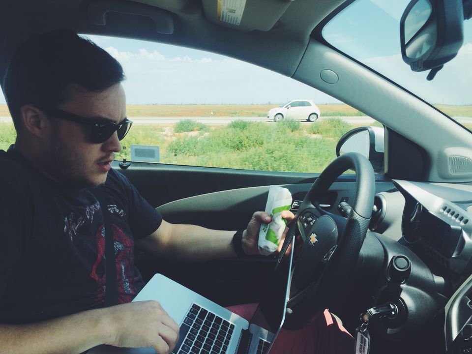 Sitting behind the wheel of a car with a burrito and a laptop trying to do 3 things at once.